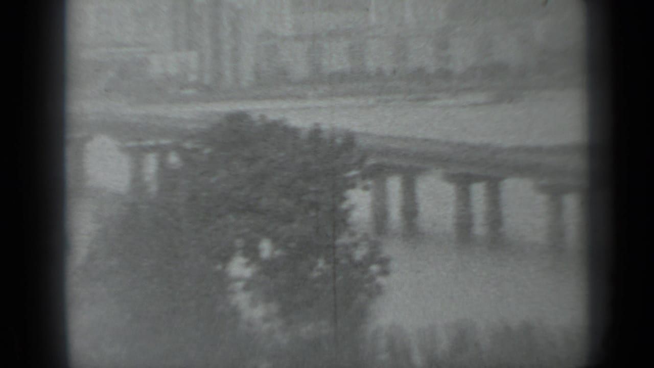 1983 Moscow home-movie frame showing a distant bridge over water, riverside trees, and soft film-gate edges.