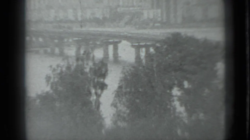 Black-and-white 8mm frame of a Moscow river bridge with trees near the water and a muted distant bank.