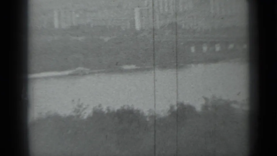 Soft black-and-white Moscow river view from 1983, with low embankment lines, foreground foliage, and visible film scratches.