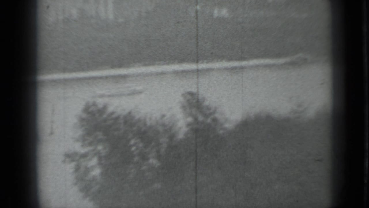 Black-and-white 8mm view across a Moscow waterway toward trees and a low pale embankment, with scratches and soft focus.
