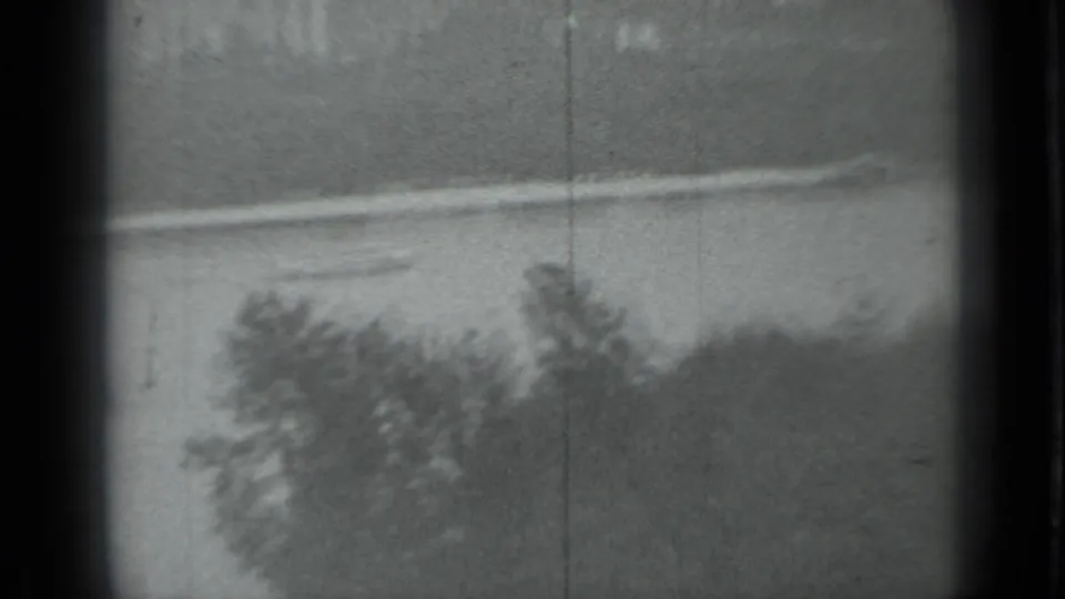 Black-and-white 8mm view across a Moscow waterway toward trees and a low pale embankment, with scratches and soft focus.