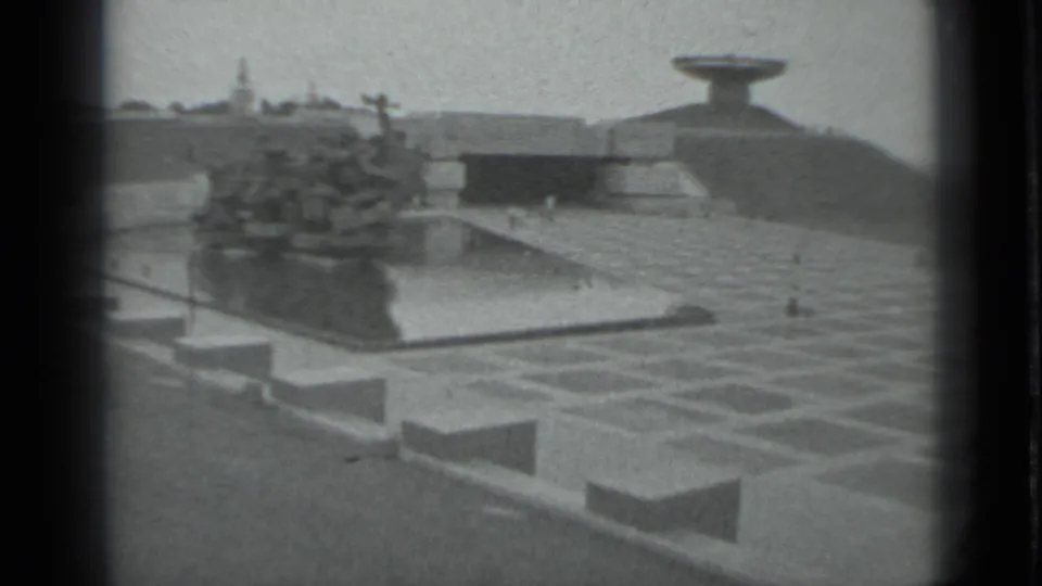 1983 Moscow 8mm frame showing a riverfront with a vessel or platform near the water, paved embankment, and distant built forms.