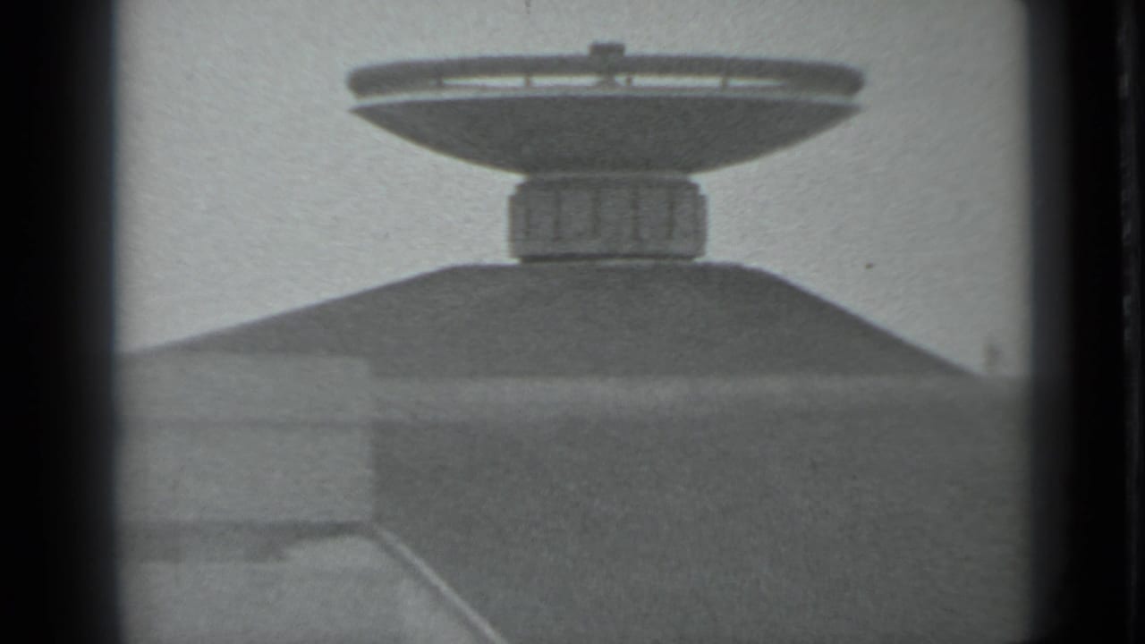 Closer black-and-white view of a dish-shaped monument mounted above a mound.