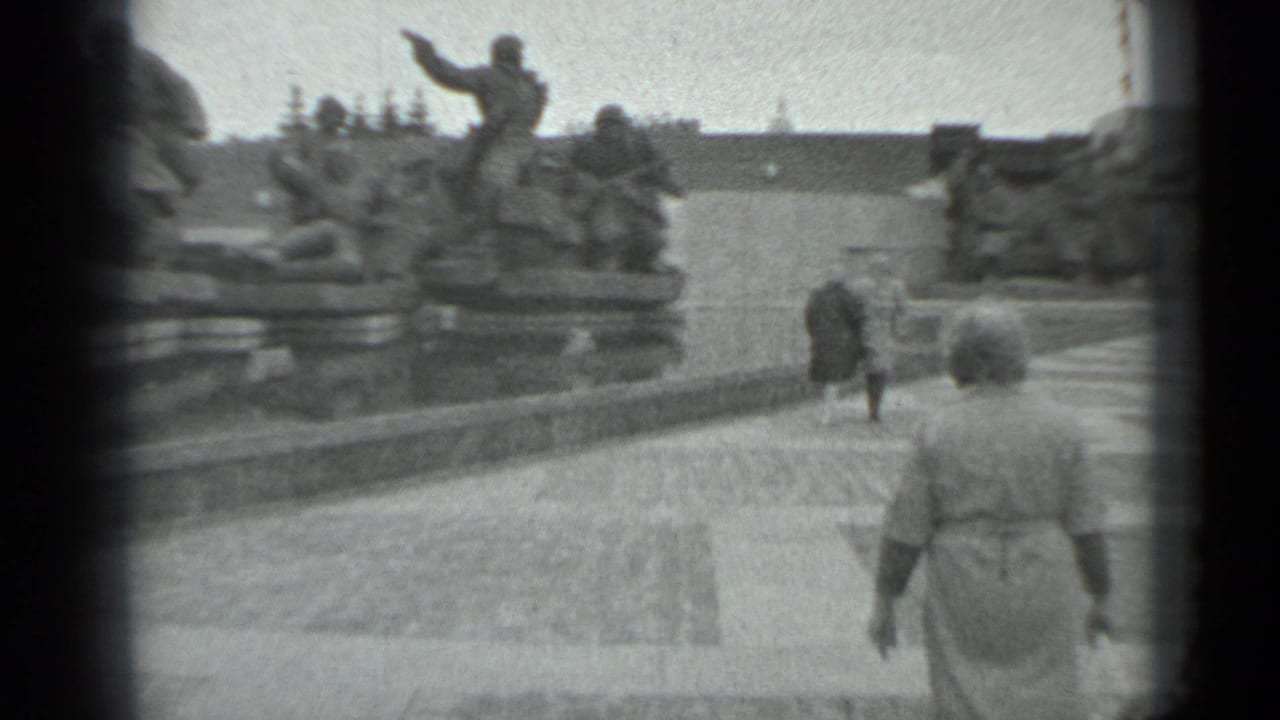 Woman carrying a small bag walks through a Moscow plaza toward a large war memorial, with visitors ahead.