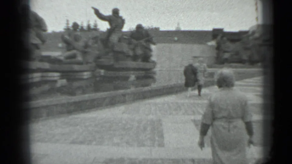 Woman carrying a small bag walks through a Moscow plaza toward a large war memorial, with visitors ahead.