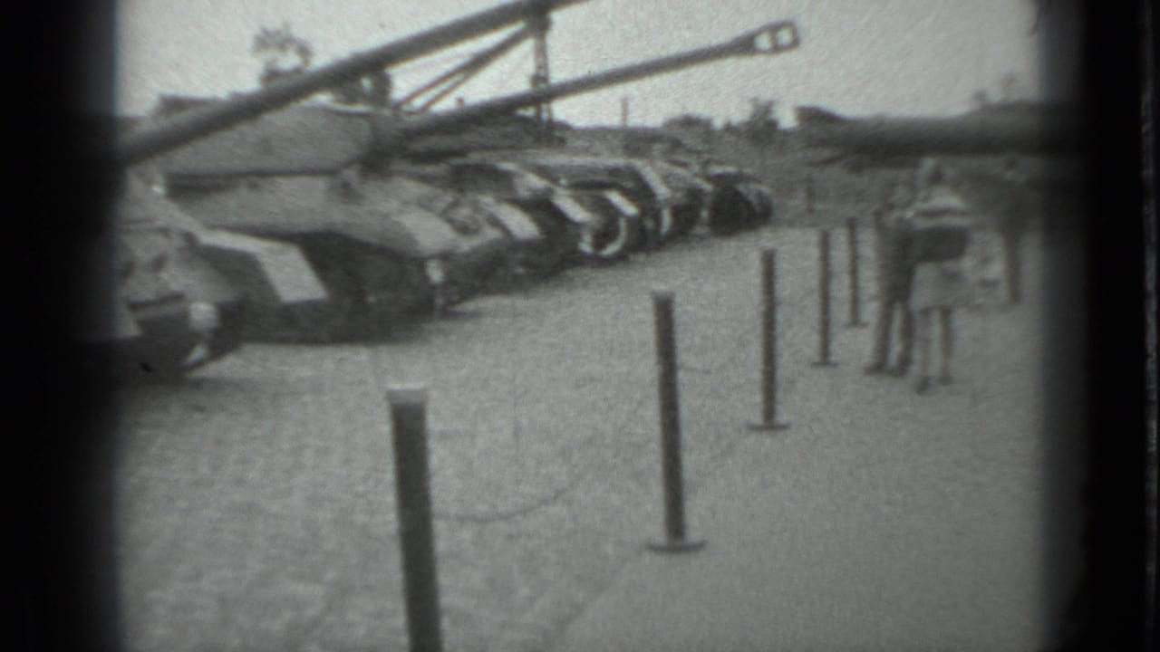 Row of tanks behind stanchions on a paved outdoor display area.