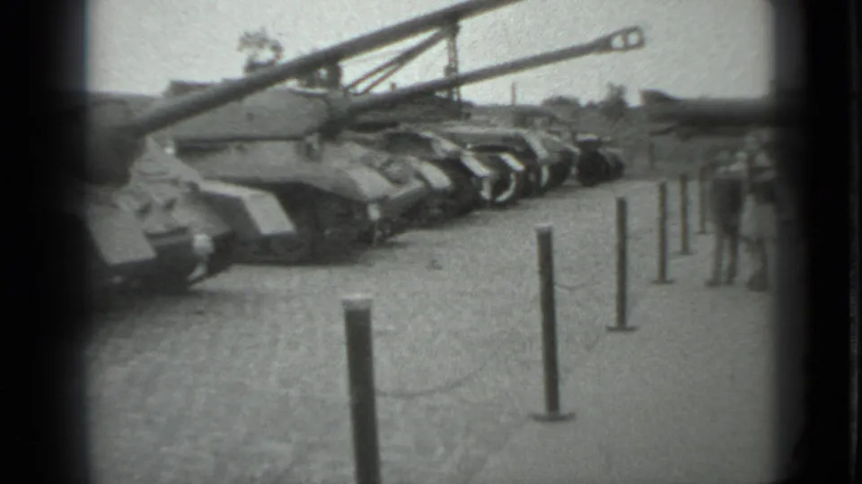 1983 Moscow frame with armored tanks displayed outdoors as civilians stand near the barrier at the edge of view.