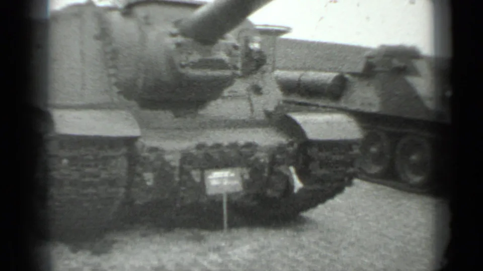 1983 Moscow home-movie frame showing a Soviet-era tank or armored vehicle on exhibition, with gun barrel, tracks, and placard visible.