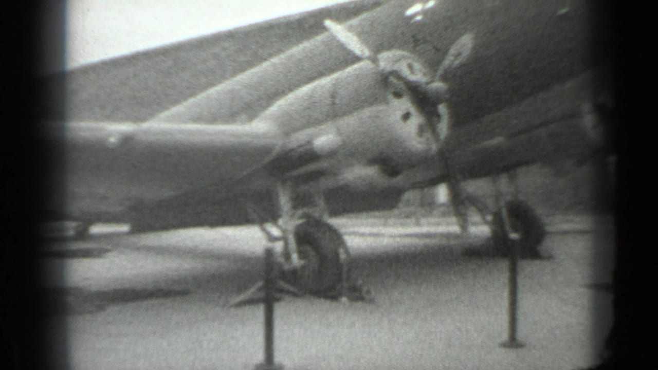 Propeller-driven military aircraft parked behind stanchions on paved ground.