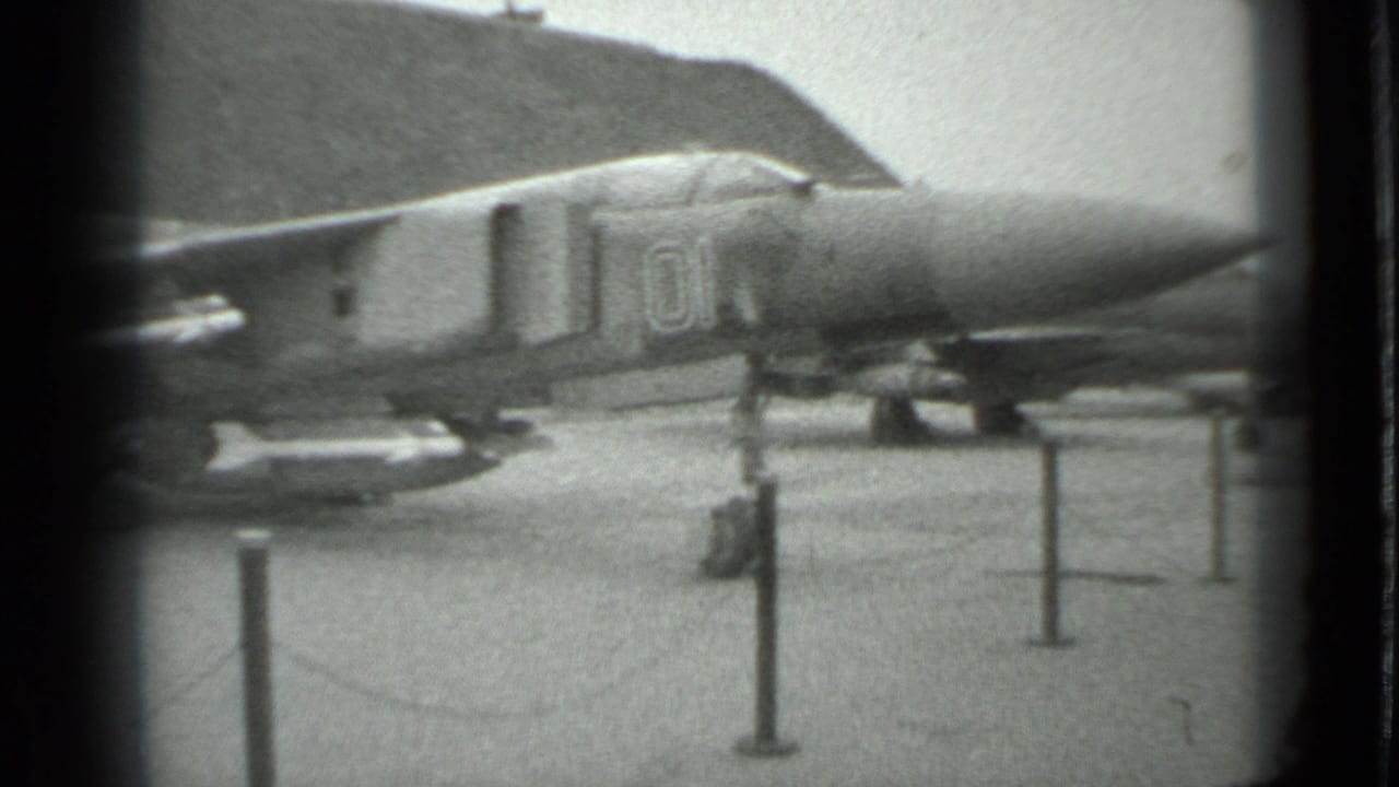 1983 Moscow 8mm frame showing the forward section of a parked military jet fighter behind stanchions on paved ground.