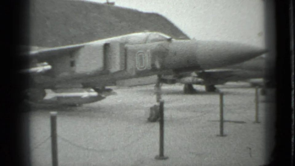 1983 Moscow 8mm frame showing the forward section of a parked military jet fighter behind stanchions on paved ground.