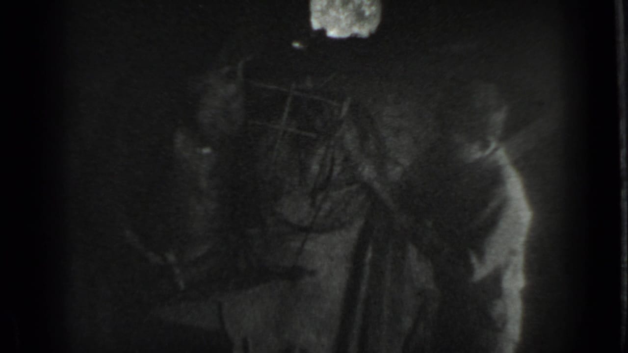 1983 Moscow home-movie frame showing a boy near an anvil or work surface in a dim workshop with heavy grain and deep shadows.
