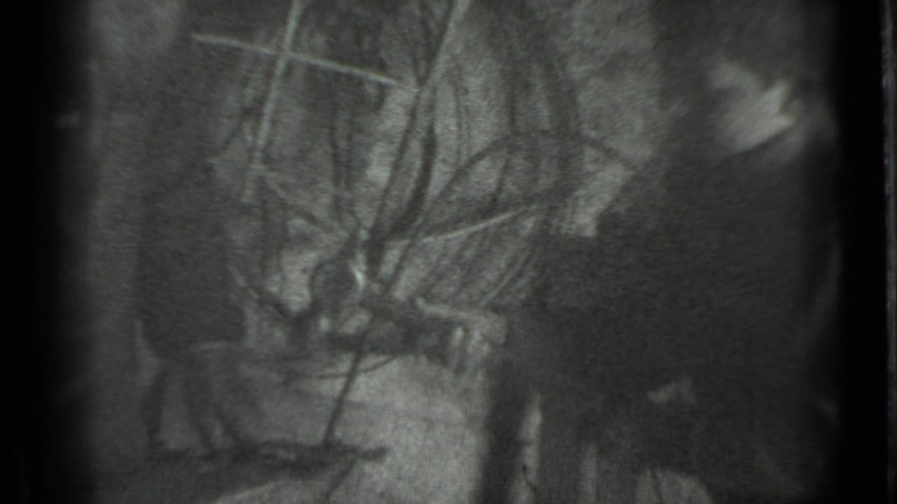 Metadata-supported Moscow 1983 home-movie frame with a partially visible person beside a dim workbench or tool area.