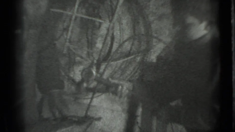 Metadata-supported Moscow 1983 home-movie frame with a partially visible person beside a dim workbench or tool area.