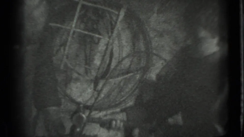 Moscow 1983 home-movie frame showing a shadowed interior with a partially visible person and indistinct tool-like objects.
