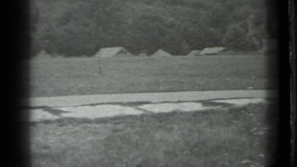 Final 1983 Moscow-region frame shifts to a distant view of simple structures across a field, with a wooded background.