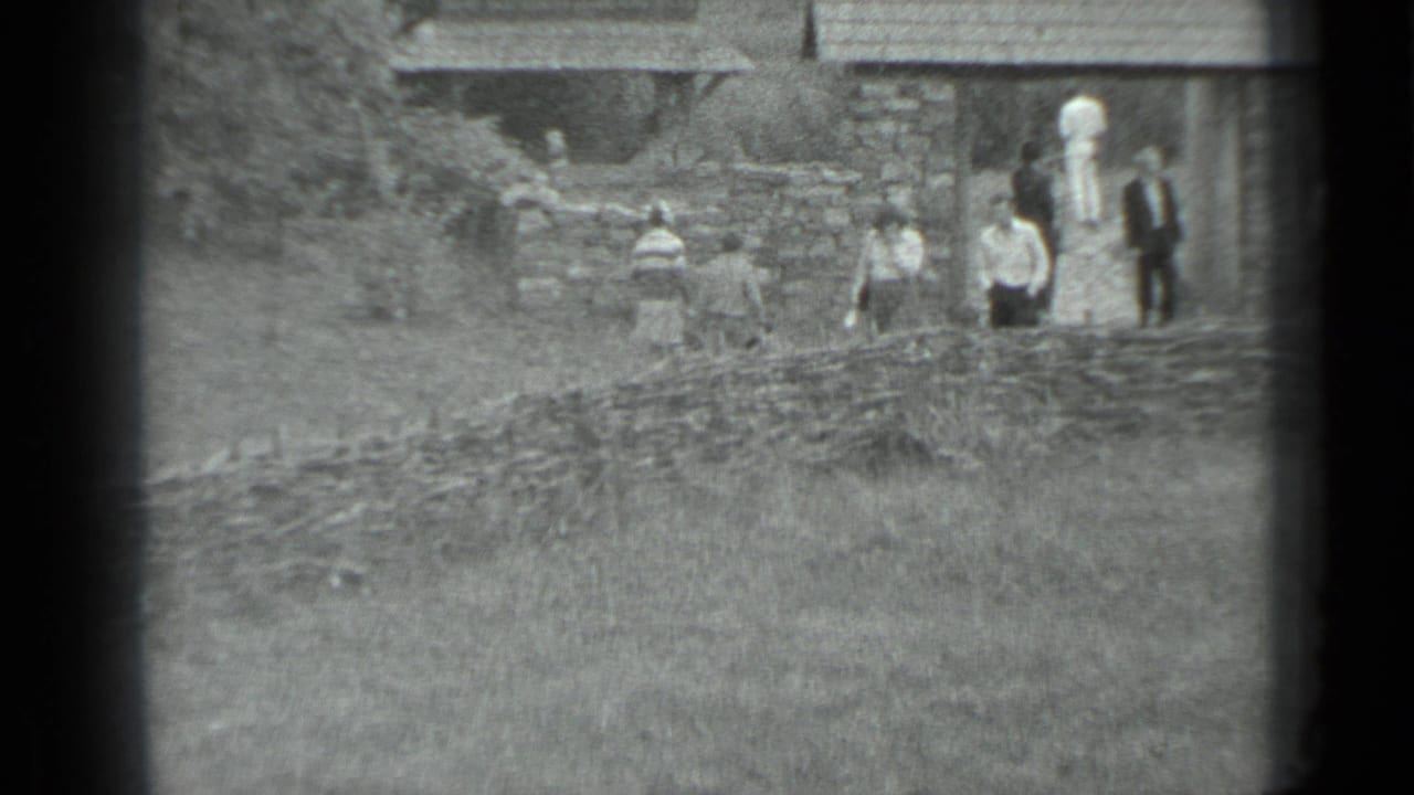 People stand and walk near stone walls and rustic village buildings.