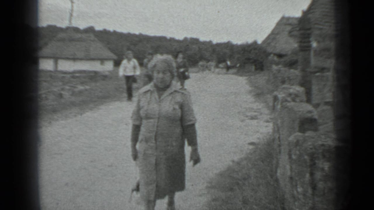 The woman continues walking toward the camera in the rural Moscow-area setting, with low walls, huts, open ground, and background pedestrians visible.