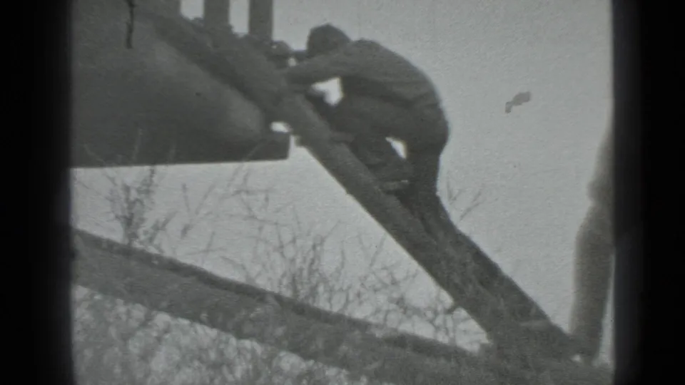 At the end of the clip, the man continues up the makeshift wooden ladder beside the log cabin, with bare branches below.