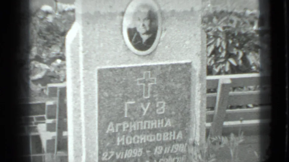 Close-up of a Cyrillic gravestone in Moscow, supported by metadata, showing an oval portrait, cross motif, and cemetery railing.