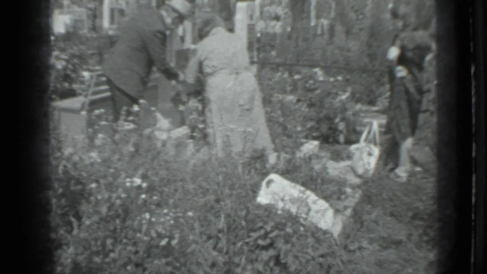 A group in 1983 Moscow appears to collect or handle debris among cemetery plants while a smaller figure stands at the edge of the plot.