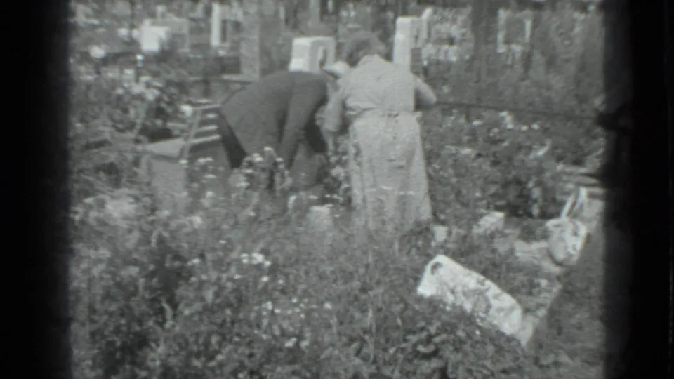In Moscow home-movie footage from 1983, an older couple tends plants among tall grass and flowers as a younger woman watches nearby.