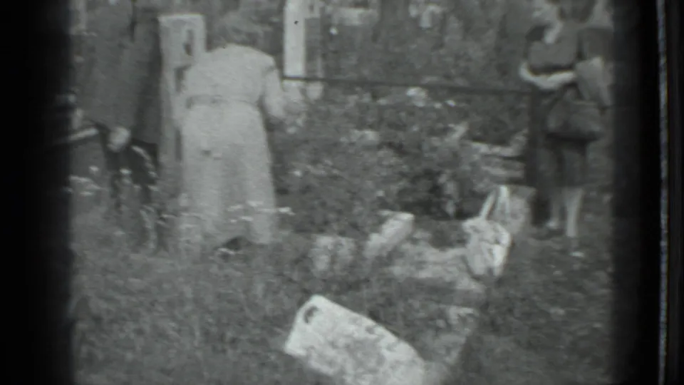 A woman in a light dress works low among the plants while a younger woman stands at the garden edge in the 1983 Moscow home movie.