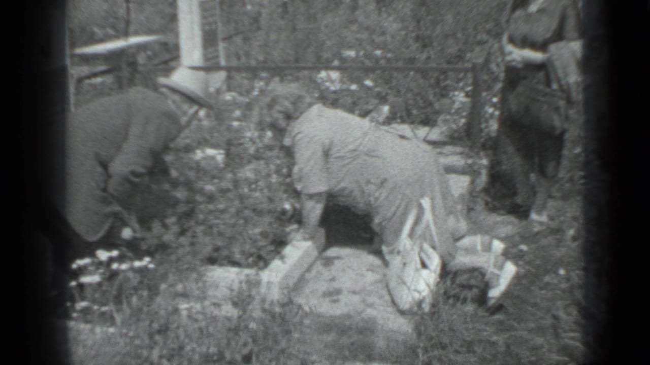 Two people bend over a flower bed while a third stands near the edge of the garden.