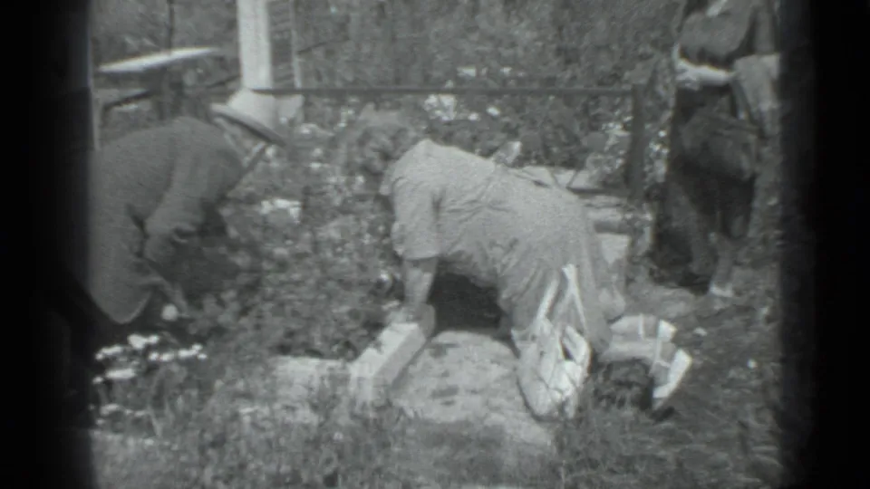 Black and white 1983 Moscow 8mm frame showing people tending a flower bed beside stone edging and garden plants.