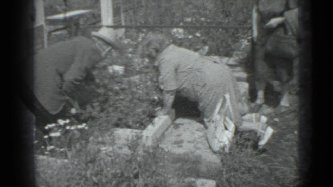 People lean into a garden bed with flowers and stone borders in a black and white frame.