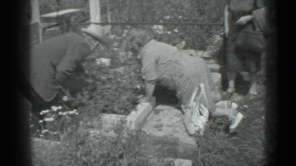 1983 Moscow home-movie frame with two people bent over garden plants and another figure partly visible nearby.