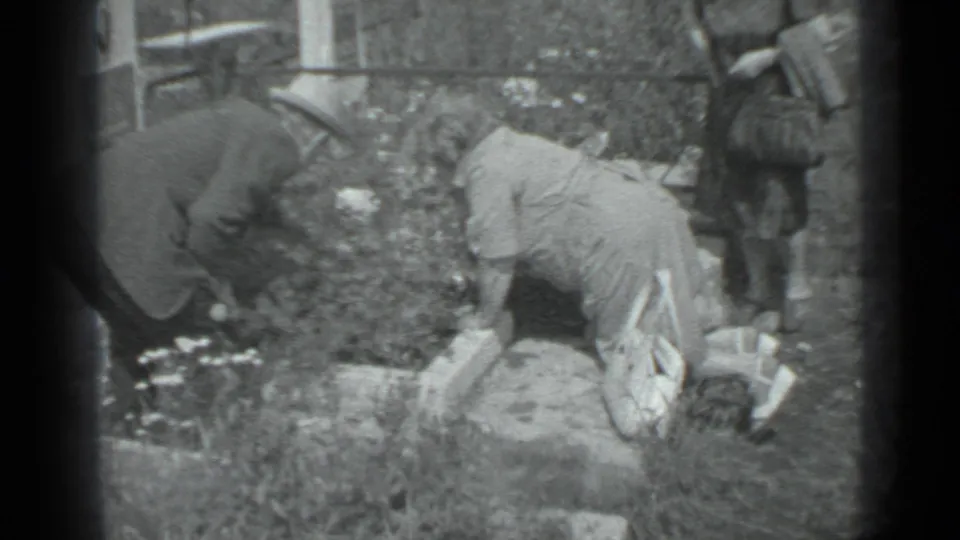 Black and white 8mm still from Moscow in 1983 showing garden work among flowers, grass, and stone borders.