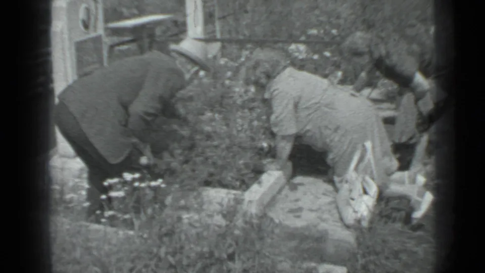 1983 Moscow 8mm frame showing three people around a domestic garden bed with flowers, grass, and stone edging.