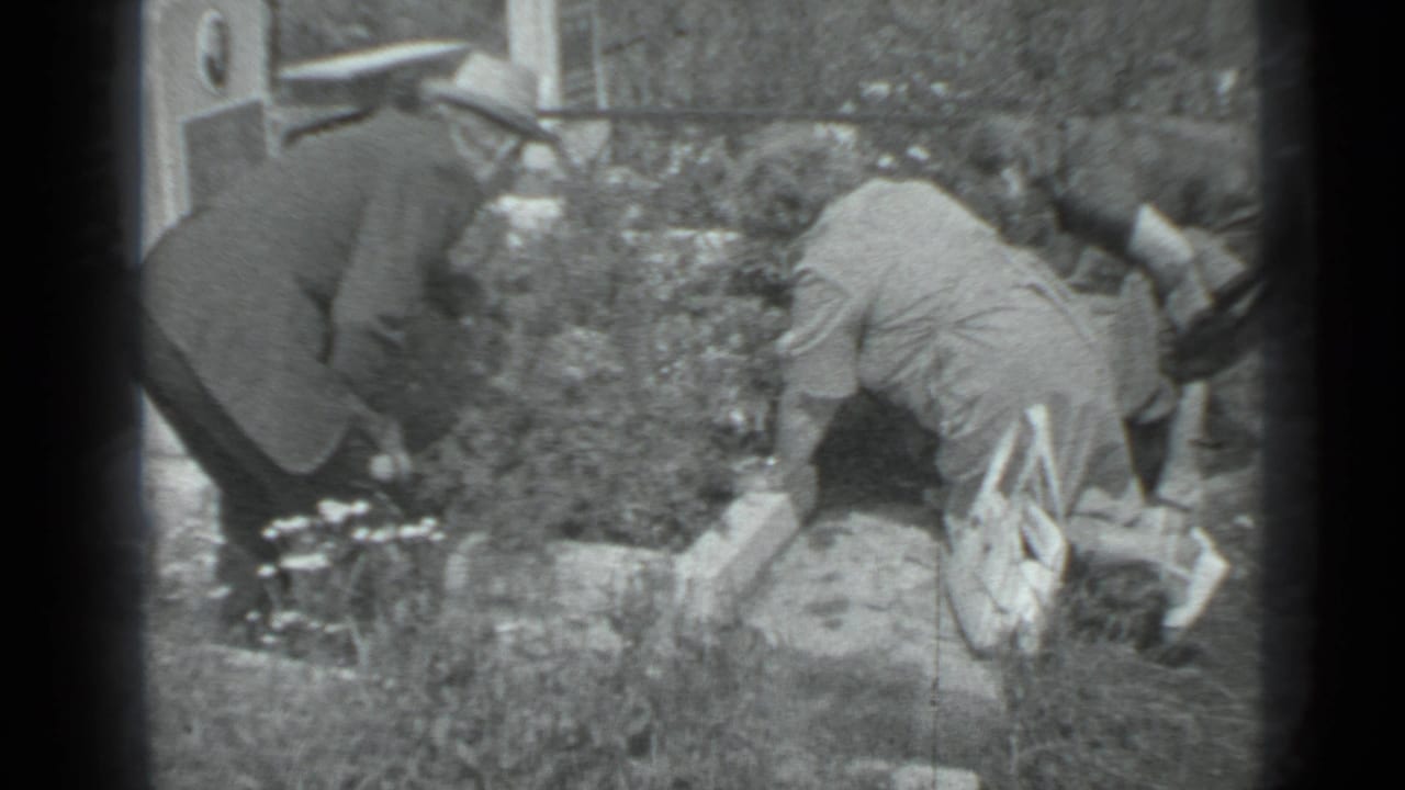 Adults tending flowers at a grave in a cemetery garden.
