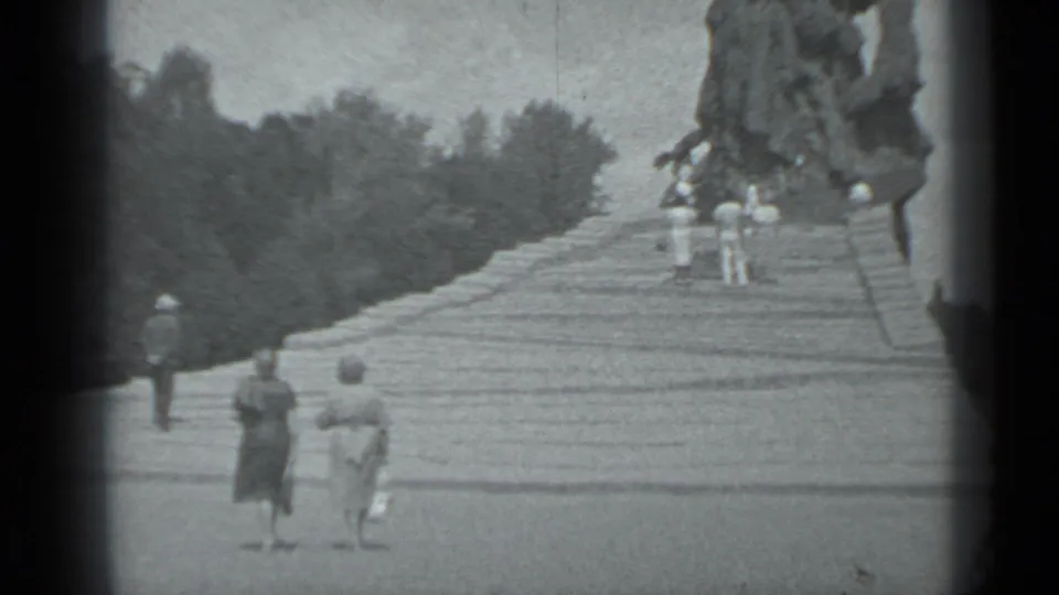 Several visitors in 1983 Moscow walk up wide stone steps toward a large sculptural monument in a landscaped setting.