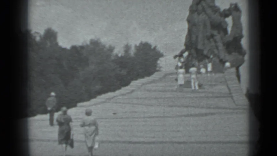 Moscow home-movie frame showing visitors on broad steps below a towering statue, with trees along the left background.