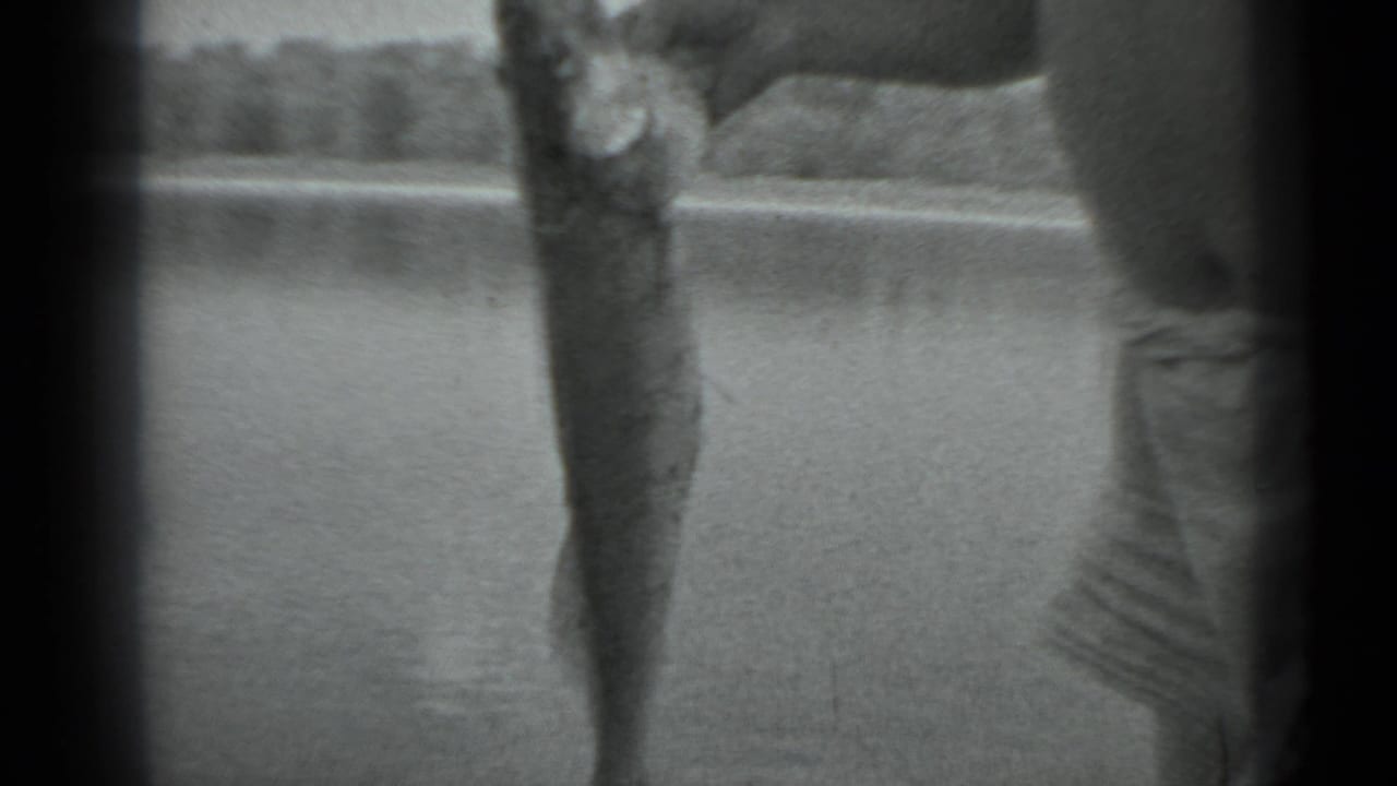 A close handheld view shows the caught fish held upright beside the man, with lake water behind him.