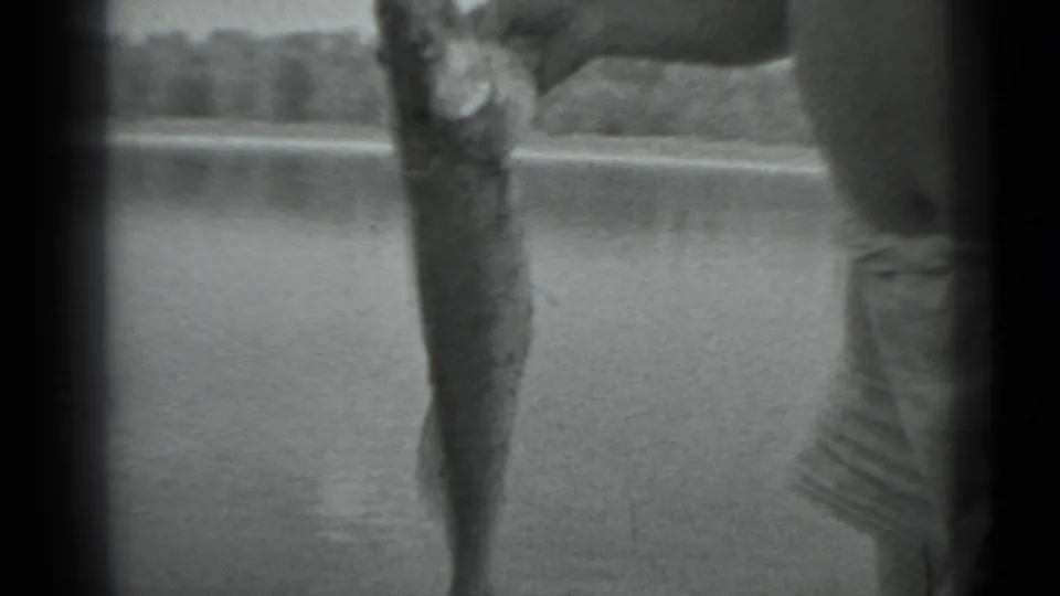 A close handheld view shows the caught fish held upright beside the man, with lake water behind him.