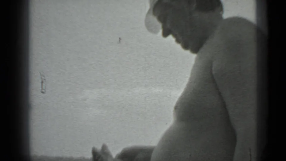 A shirtless man in a brimmed hat is seen in profile near the lake, looking down toward the catch or shoreline.