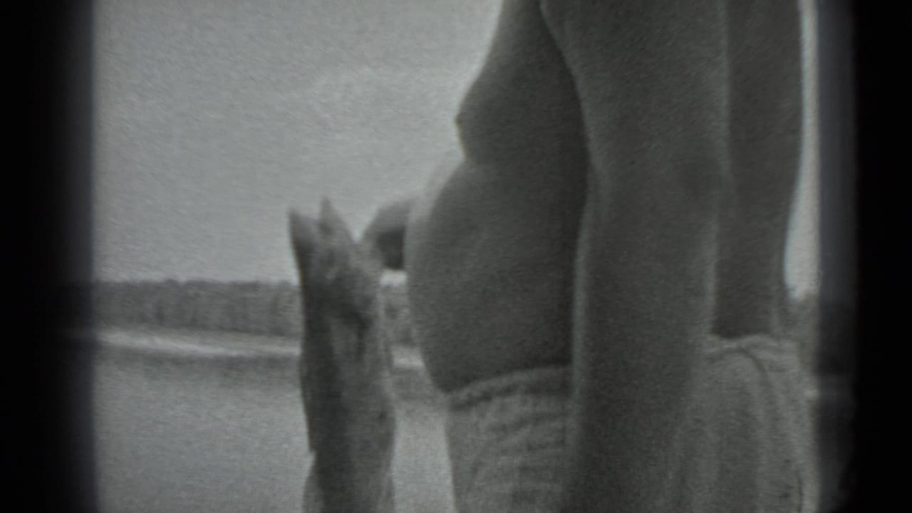 In 1983 Moscow home-movie footage, an adult man in swim trunks stands near lake water holding a large fish upright.