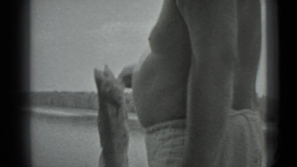 In 1983 Moscow home-movie footage, an adult man in swim trunks stands near lake water holding a large fish upright.
