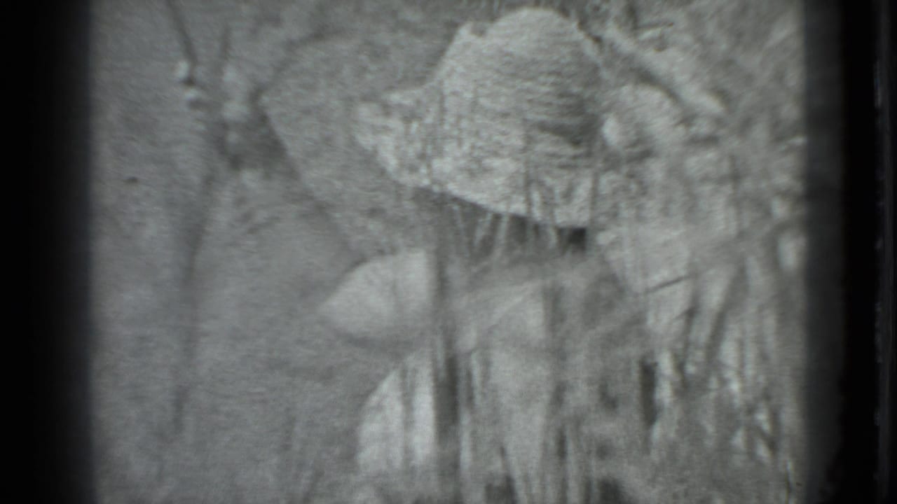 A woman in a wide-brimmed hat appears behind tall grass in black-and-white 1983 Moscow home-movie footage.