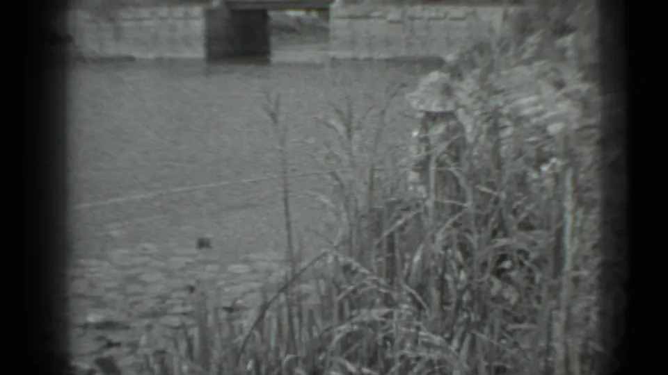 Black-and-white 8mm view of Moscow pond water, reed growth, and a bridge support framed by visible film borders.