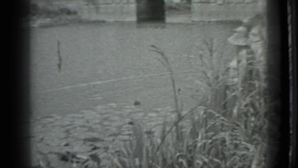 1983 Moscow 8mm frame showing canal water, reeds, stones, and a concrete bridge or culvert beyond the bank.