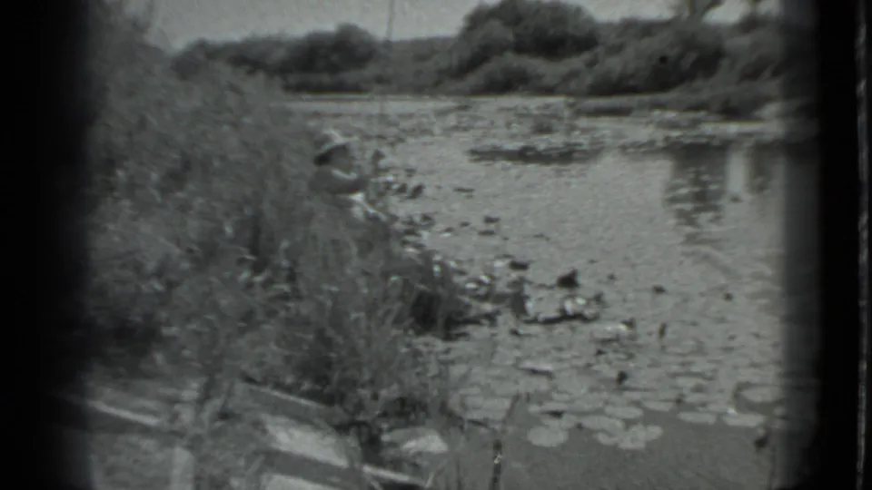 In metadata-identified Moscow, 1983, a woman in a light hat fishes from an overgrown shoreline beside a small lake.