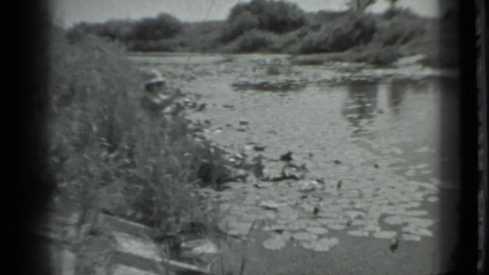 The woman remains on the grassy bank, facing the small lily-pad-covered lake in the metadata-supported 1983 Moscow scene.