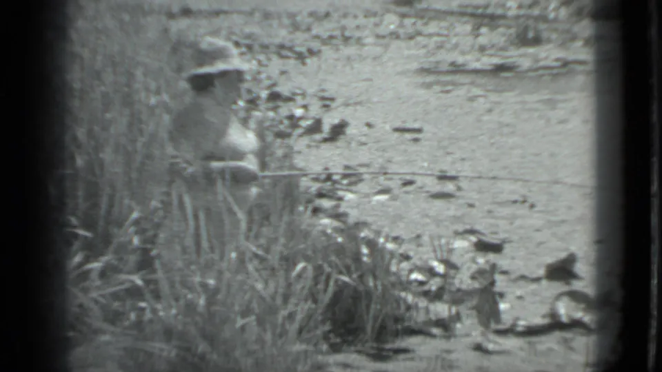 The woman stands among tall grasses at the Moscow riverbank, with a fishing line or rod extending across the frame toward the water.