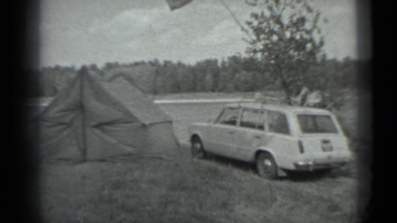 1983 Moscow-area 8mm frame showing a canvas tent and white station wagon on grass near a lake and forested shore.