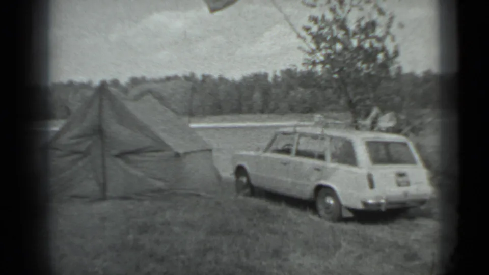 1983 Moscow-area 8mm frame showing a canvas tent and white station wagon on grass near a lake and forested shore.