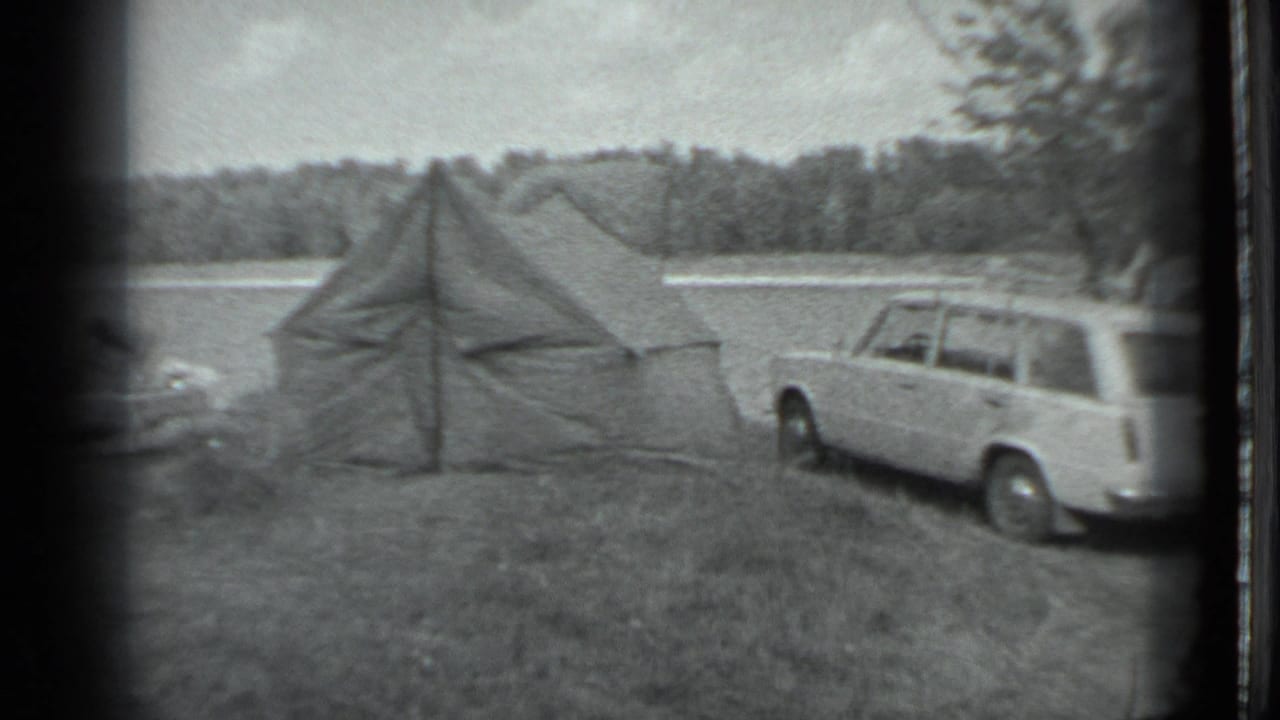 Canvas tent and station wagon in a grassy lakeside camping area.